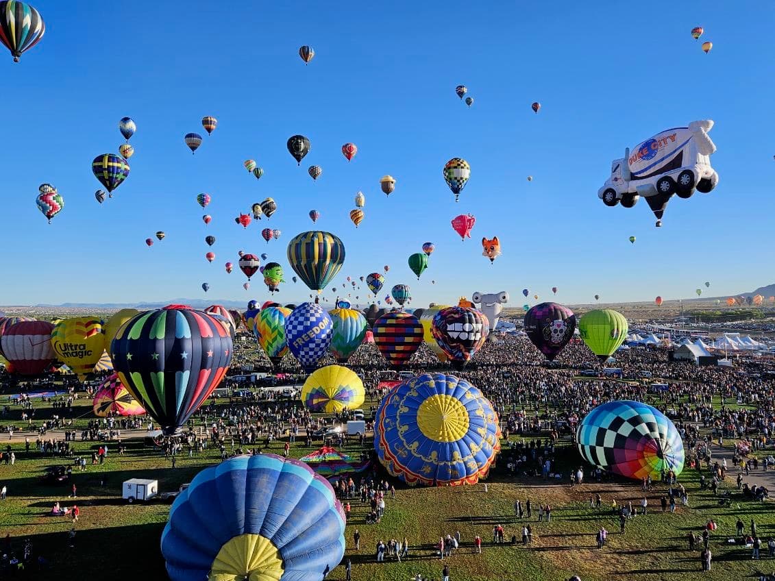 Crowd watching rows of balloons inflate at a festival launch field